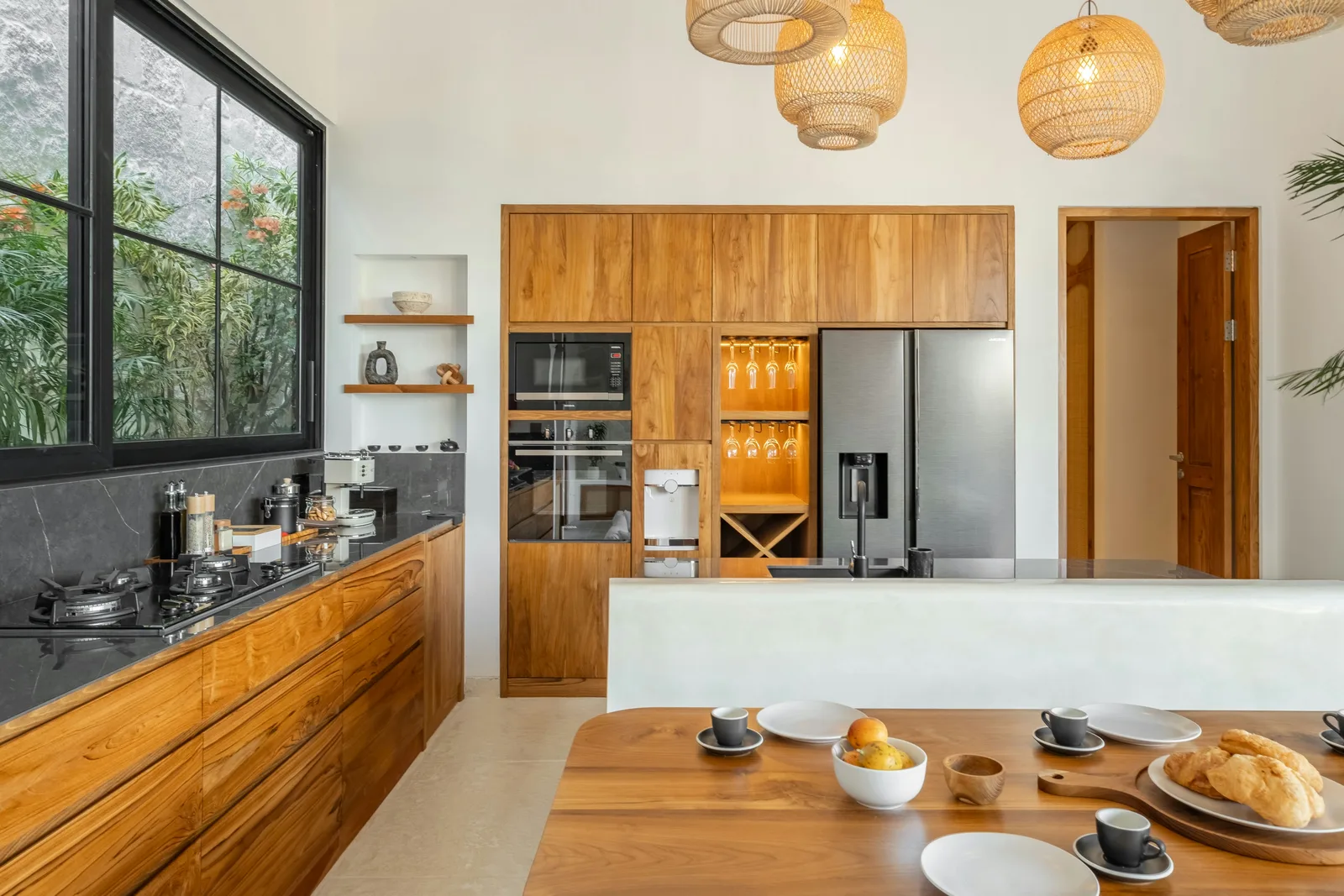 Una cocina moderna tiene armarios de madera, un refrigerador grande, una encimera oscura y una mesa de comedor.