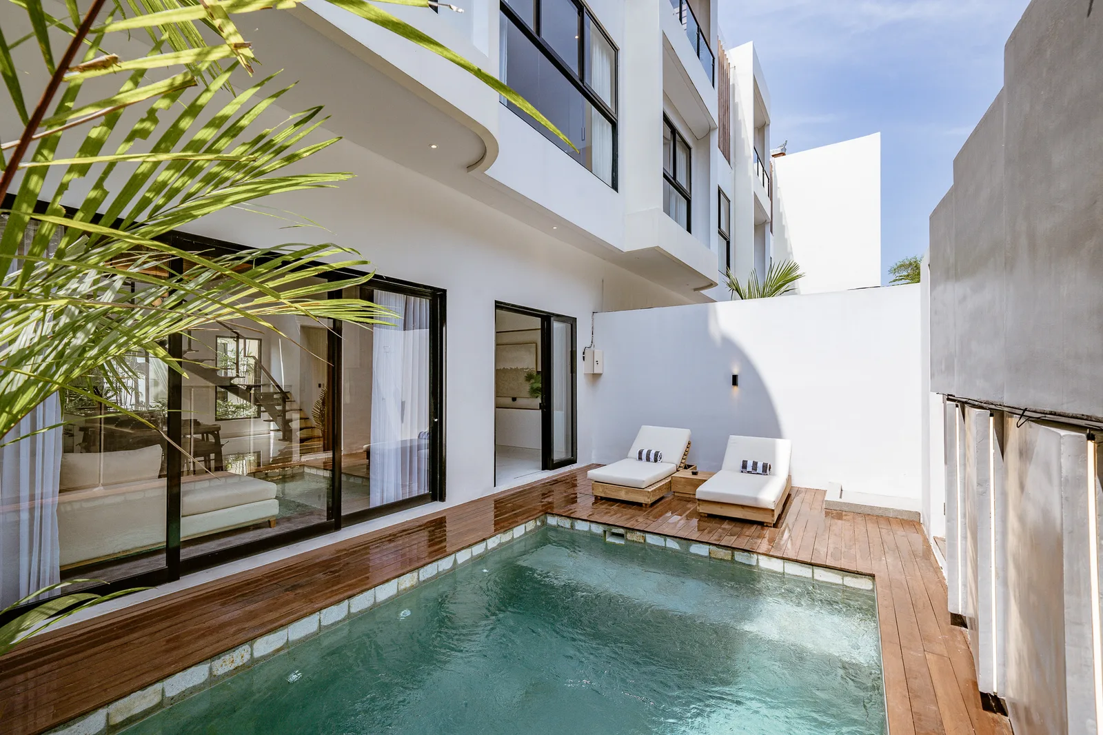 Una pequeña piscina exterior está junto a un edificio blanco moderno y una terraza de madera.