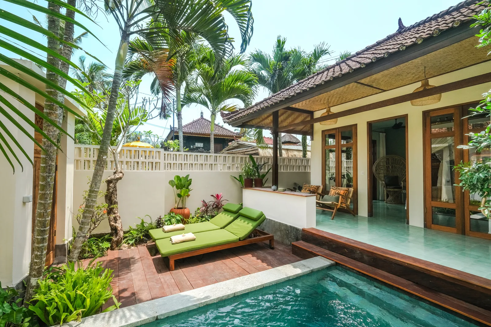 Un patio tropical con una pequeña piscina, asientos verdes y palmeras.