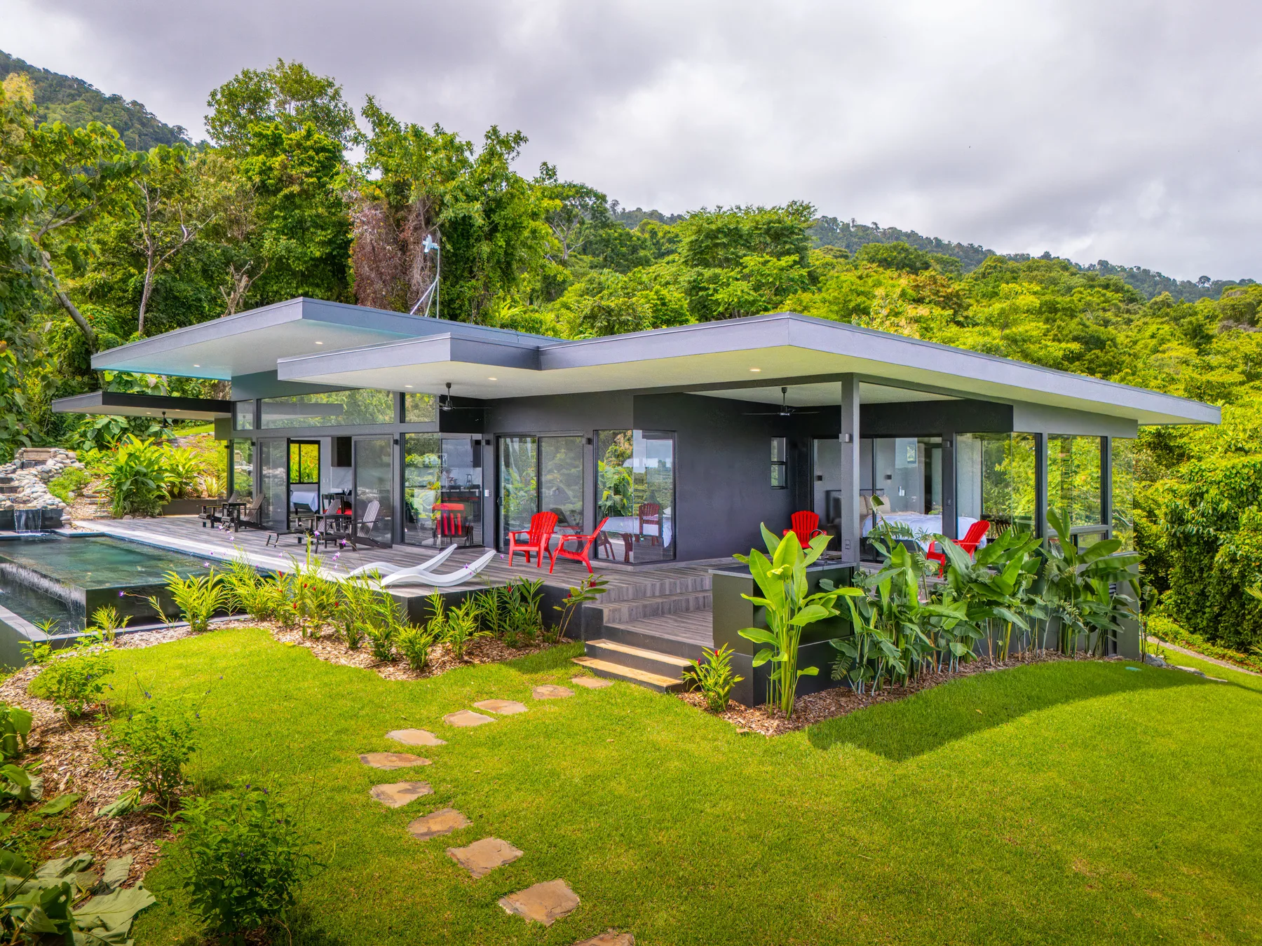Modern house with a broad roof, glass walls, and a landscaped lawn.