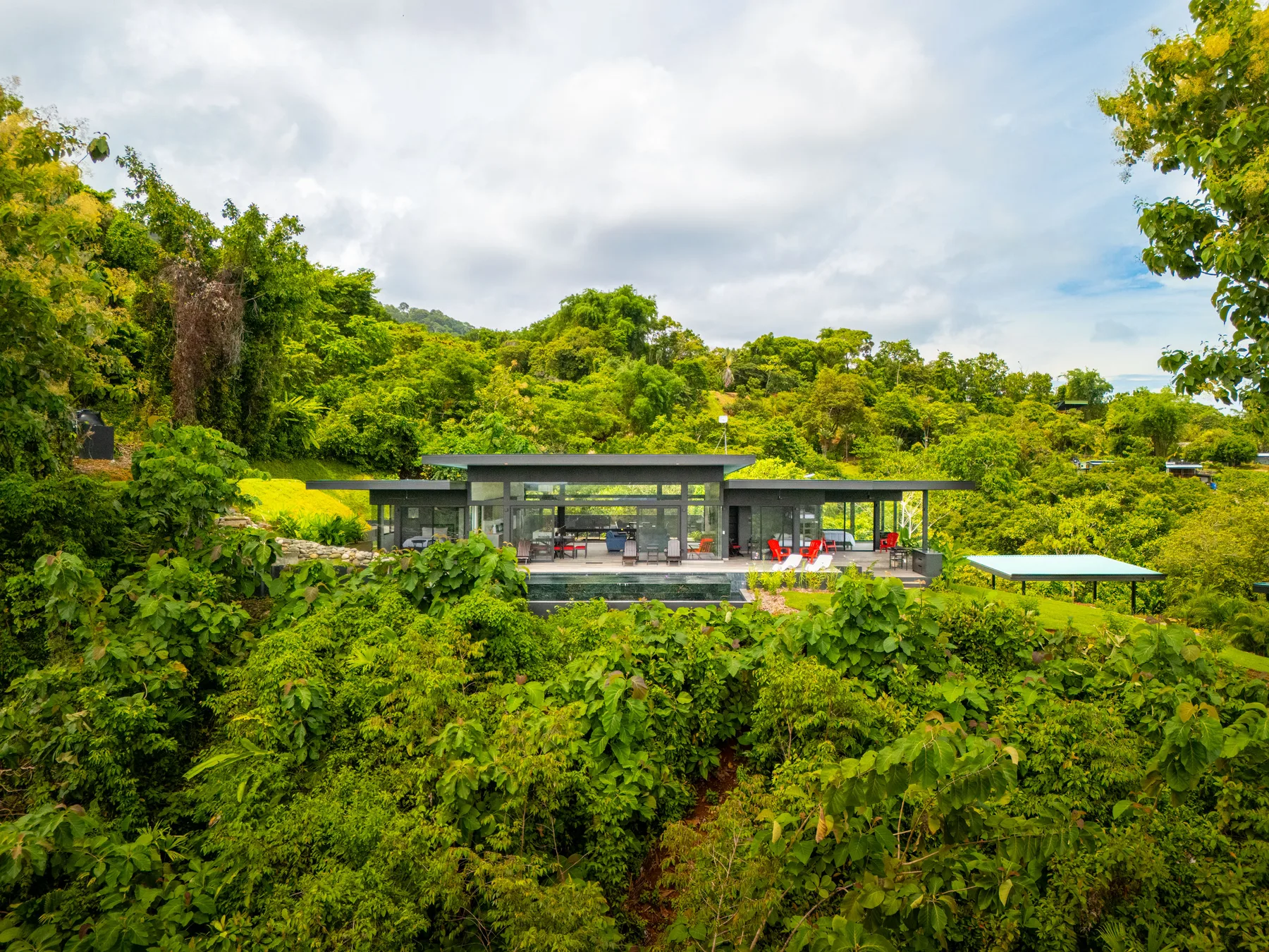 A modern glass-fronted building sits amid dense green foliage.