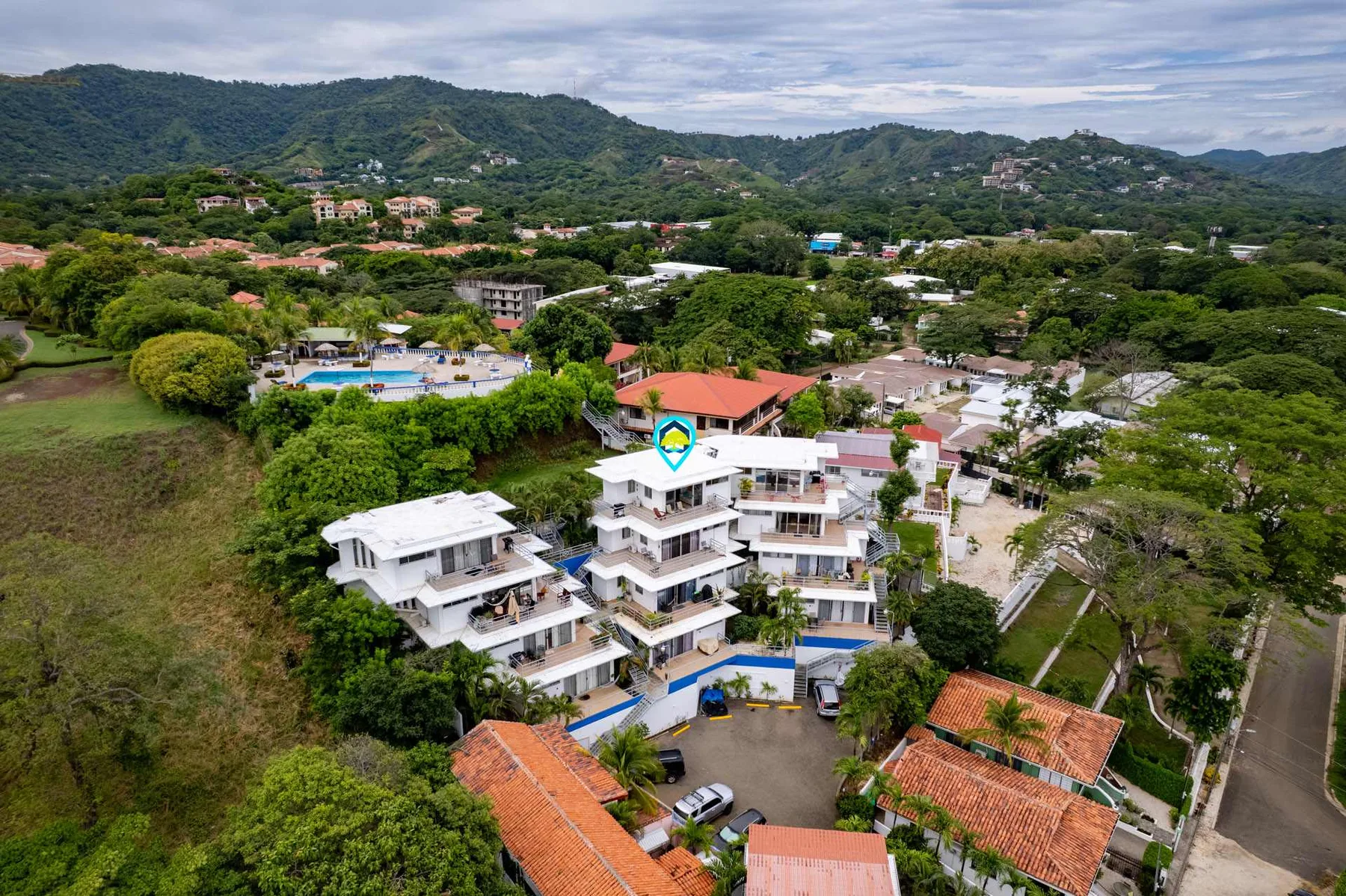 Shared amenity: Aerial view of buildings among lush greenery, with hills in the background.