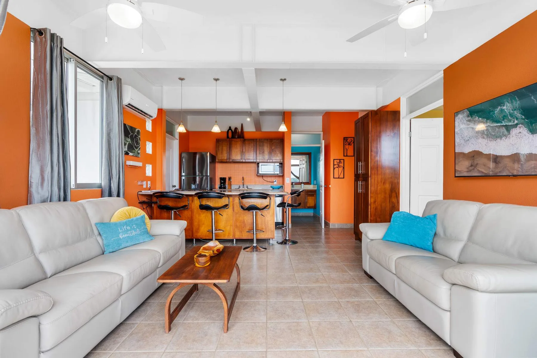 A living room opens into a kitchen, with light-colored seating and a dining counter.