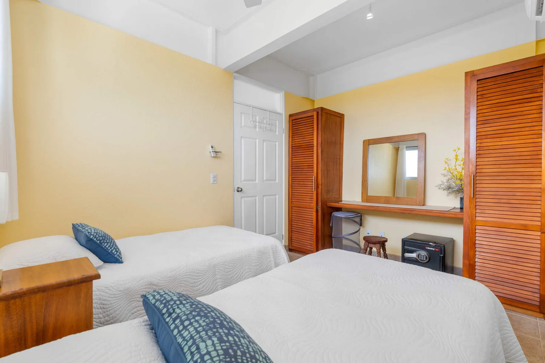 A bedroom with two beds, wooden wardrobes, and a vanity mirror.