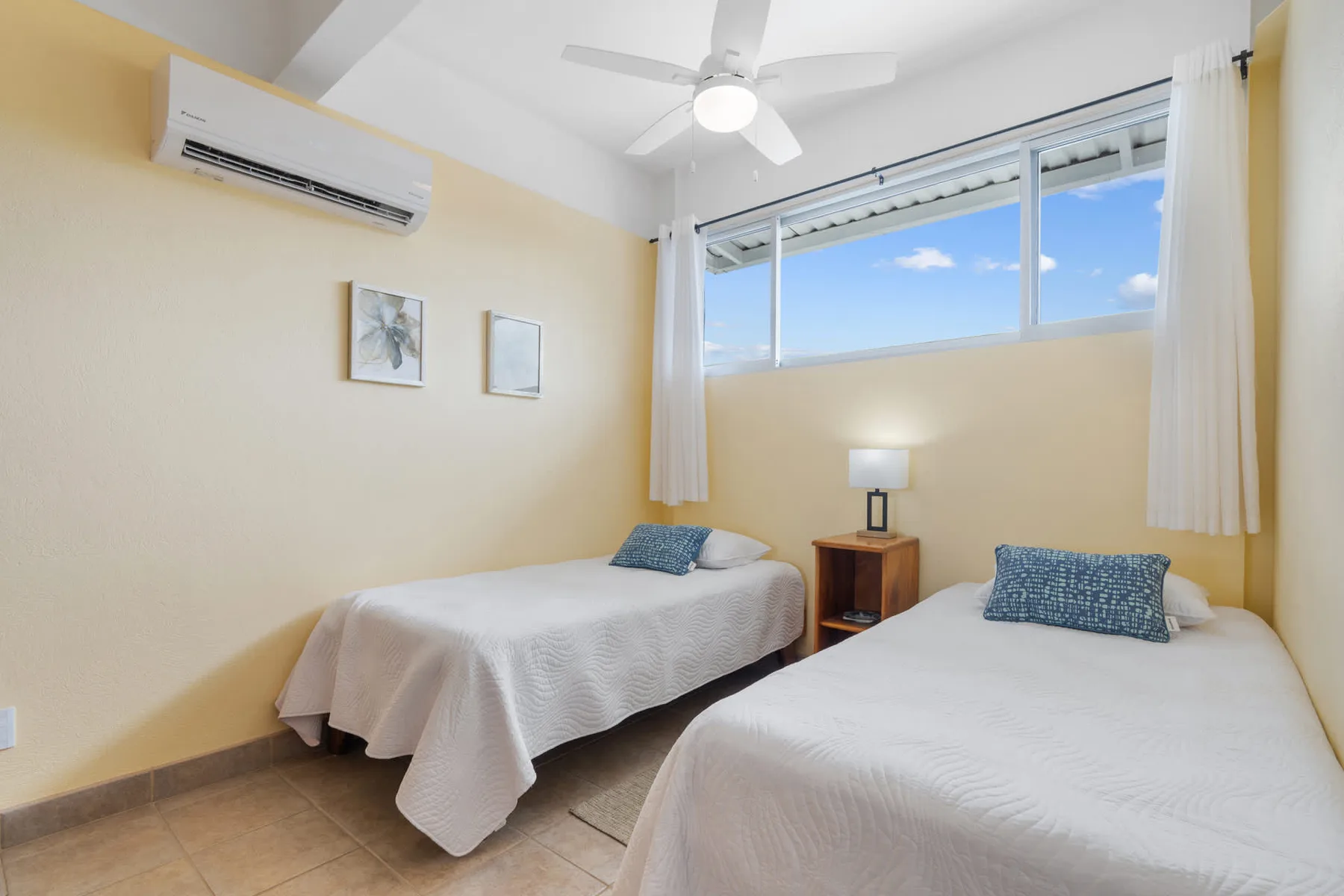 A bedroom with two beds and a bedside table beneath a large window.