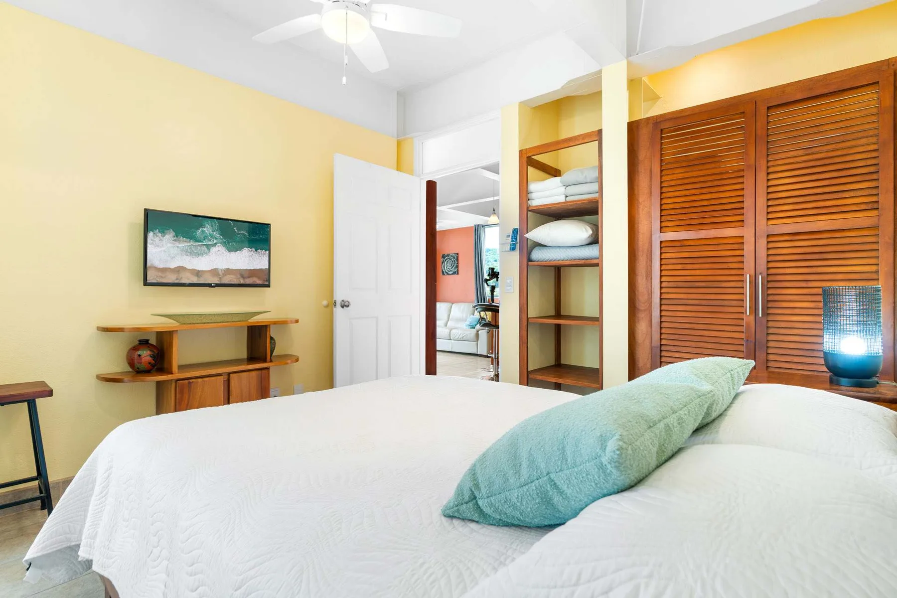 A bright bedroom with a neatly made bed and wooden louvered closet doors.