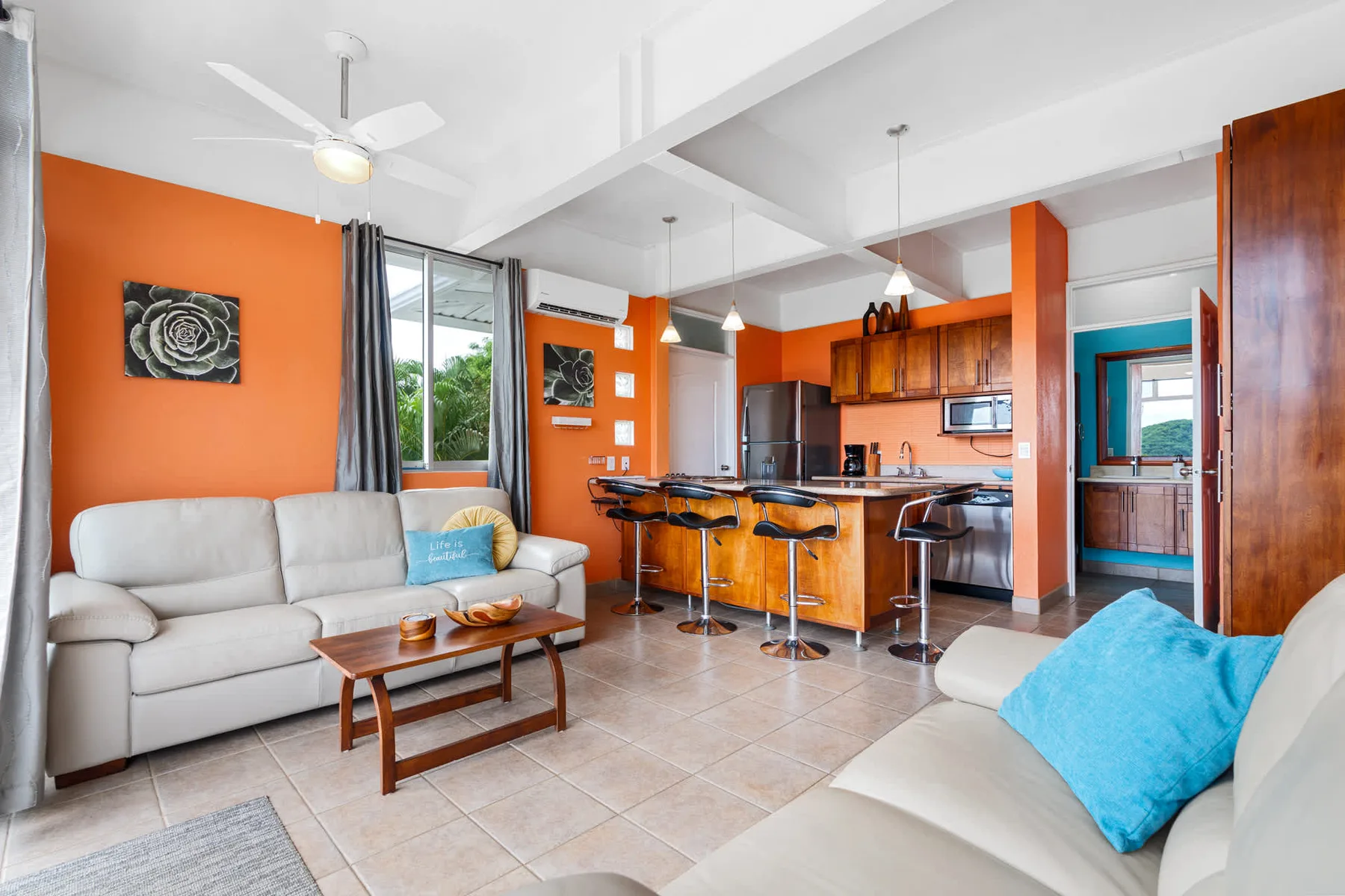 An open living room and kitchen with orange walls, wooden cabinets, and seating.