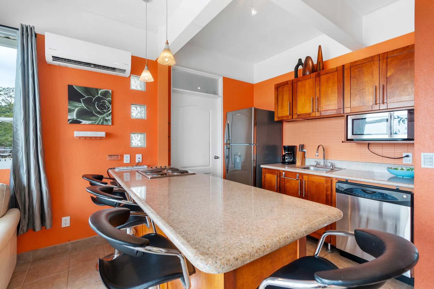 A bright kitchen with orange walls, wooden cabinets, and a large island.