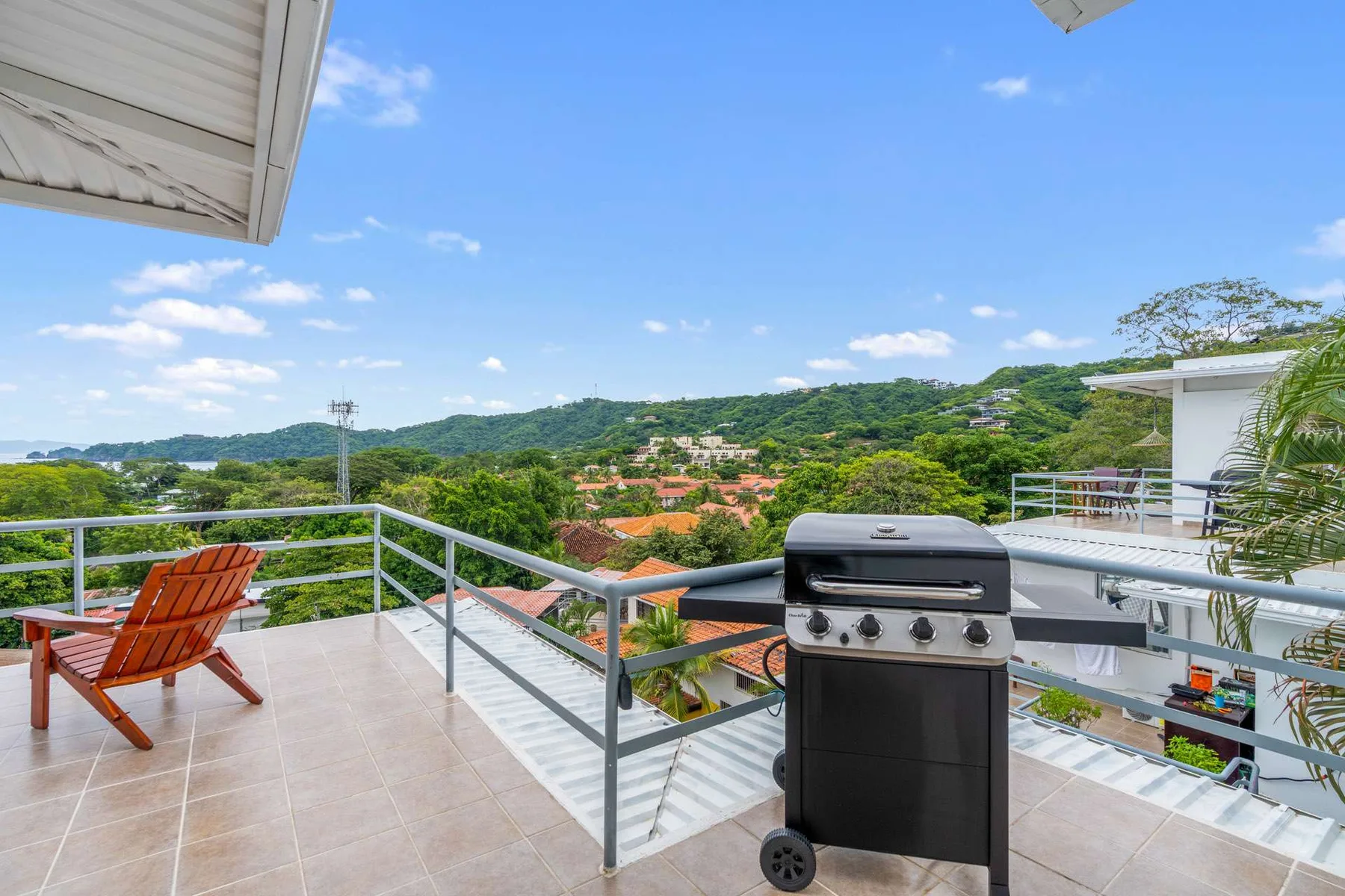 A tiled terrace overlooks green hills, with an outdoor grill beside the railing.