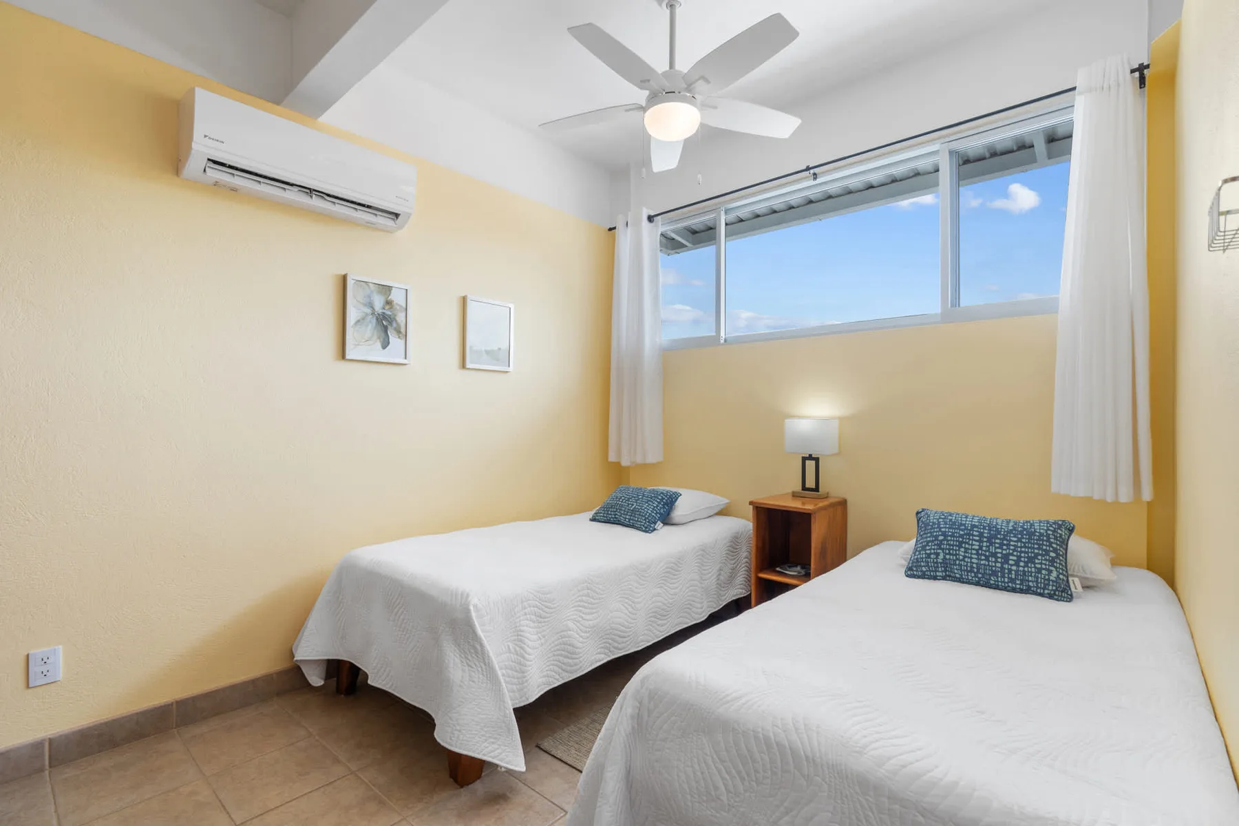 A bright bedroom with two beds beneath a wide window.
