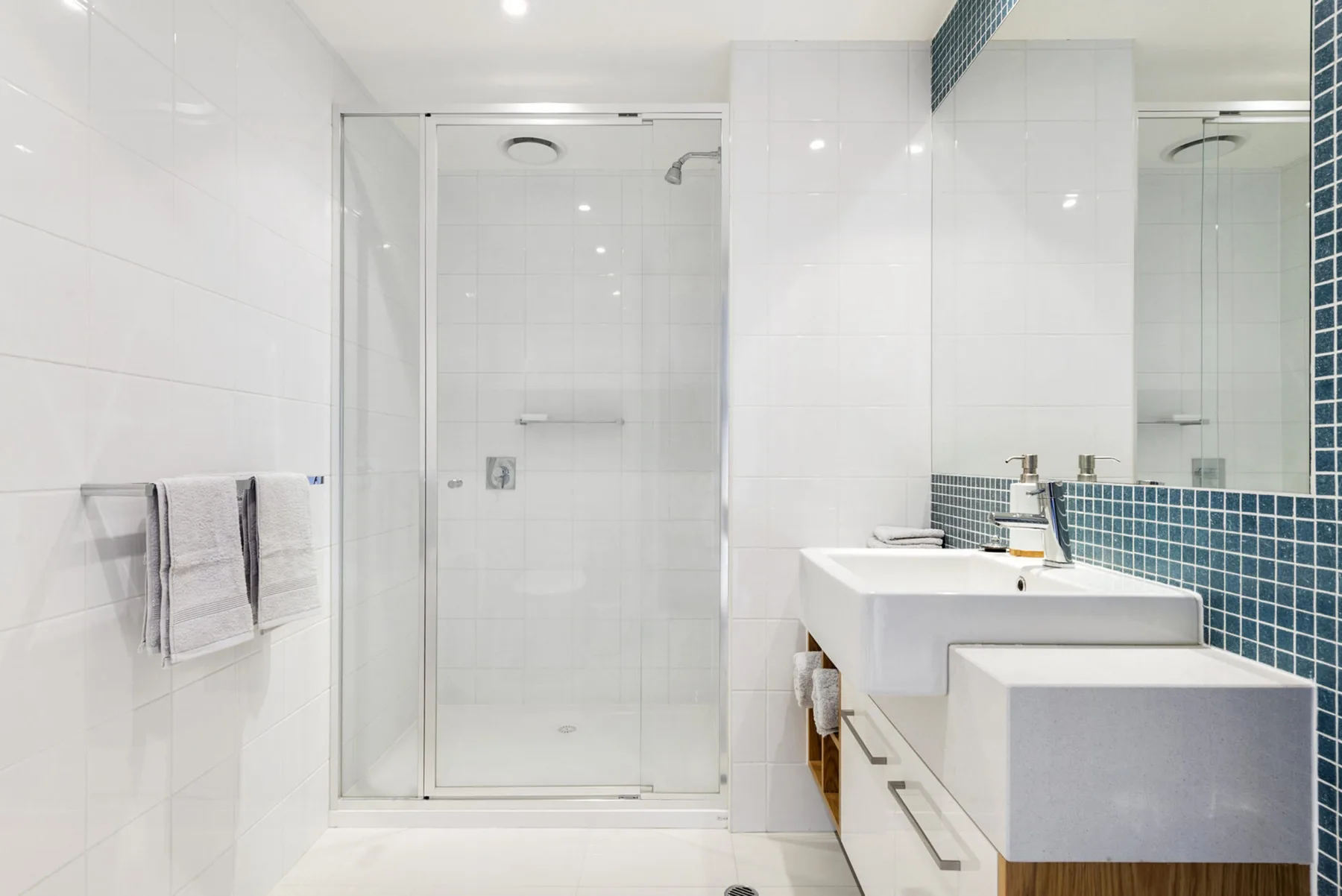 Un baño luminoso con azulejos, ducha de vidrio y lavabo.