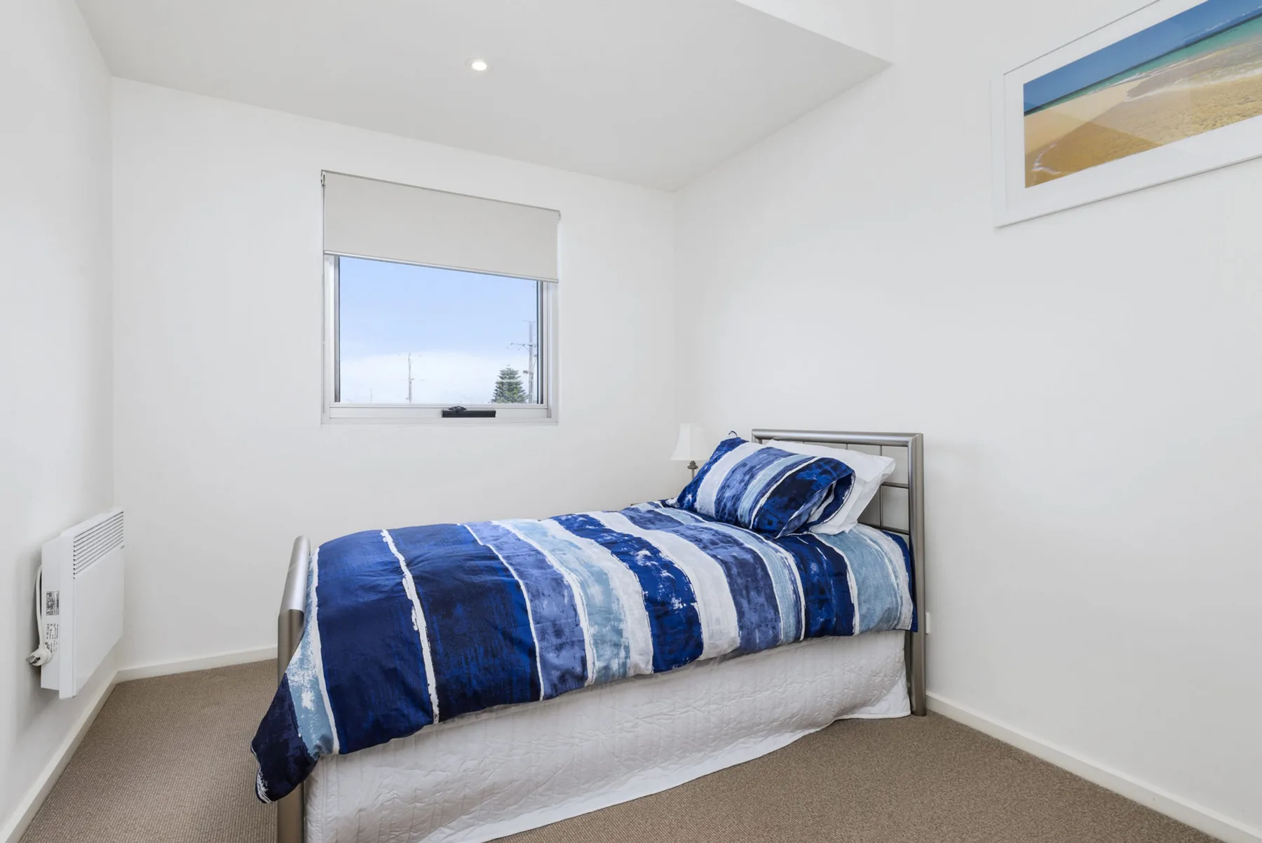 Un dormitorio luminoso con una cama cubierta con ropa de cama azul y blanca.