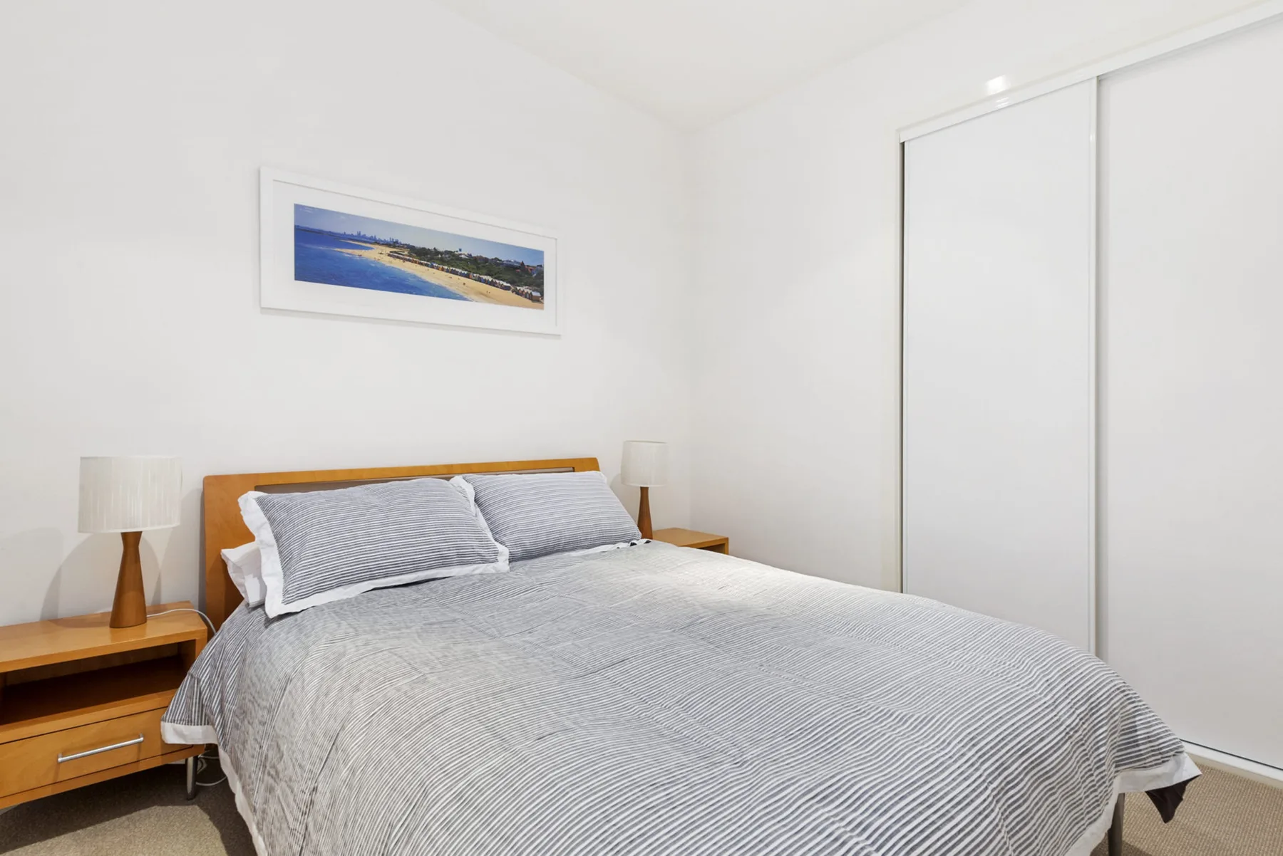 Un dormitorio con una cama vestida con ropa de cama gris y un cuadro enmarcado en la pared.