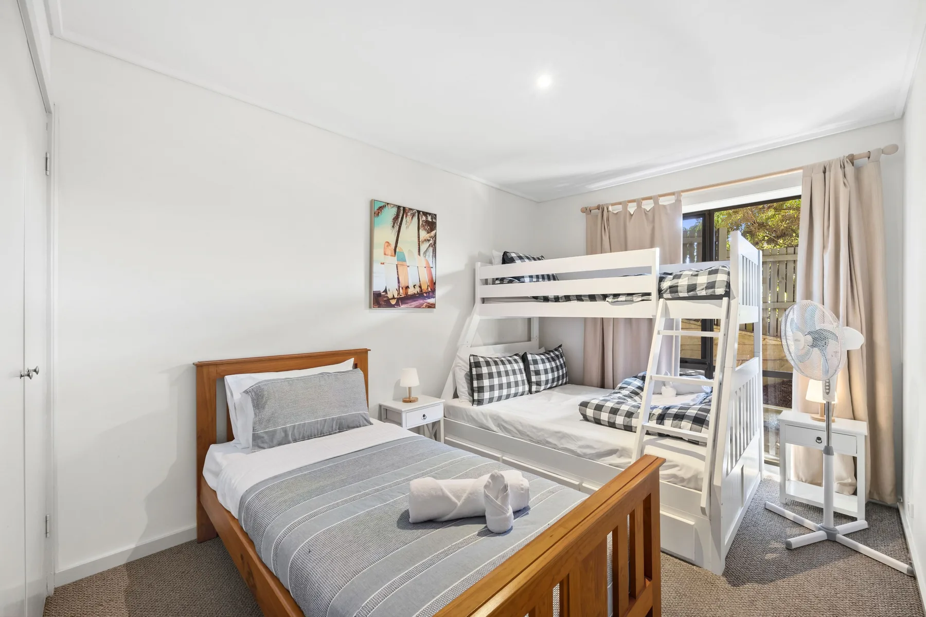 Un dormitorio luminoso con una cama de madera y una litera blanca junto a una ventana.