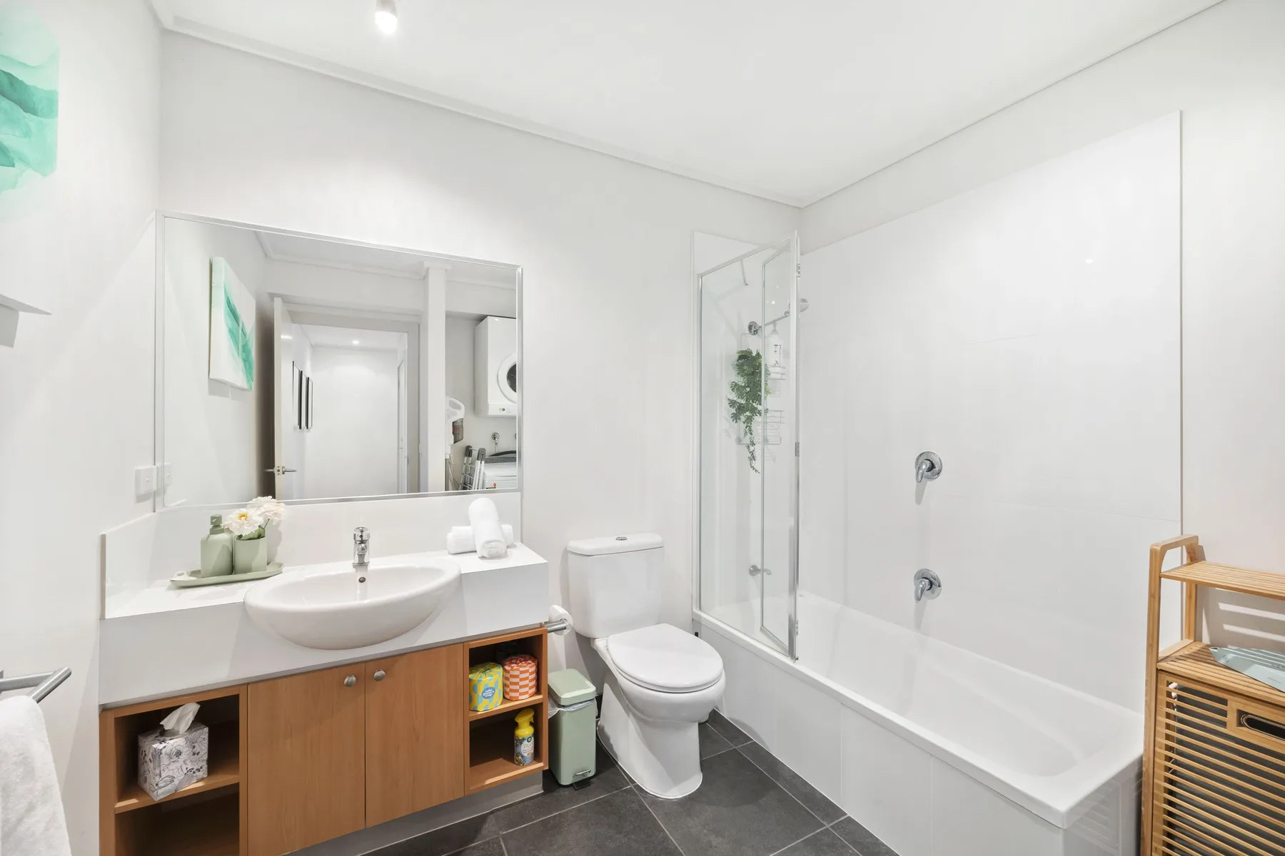 Un baño luminoso con lavabo, inodoro y bañera con mampara de vidrio.