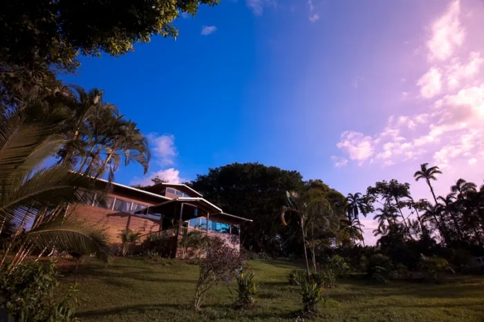 A hillside house sits among palm trees beneath a colorful evening sky.