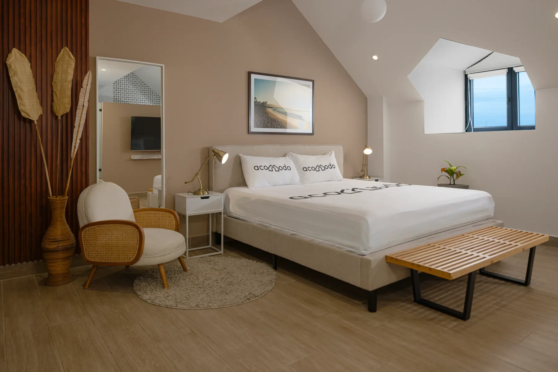 Un dormitorio con una cama grande blanca, un cuadro enmarcado y un banco de madera en el suelo.