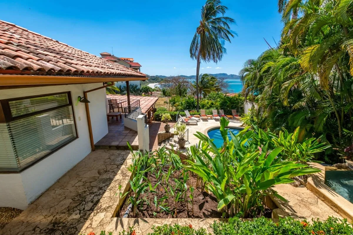 A tropical outdoor pool area beside a tiled-roof building, with ocean views.
