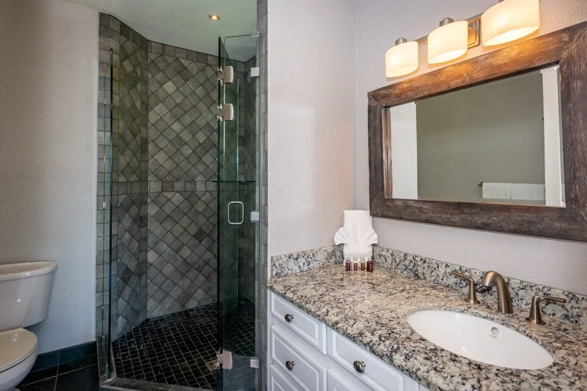 A bathroom with a glass shower and a stone counter beside the sink.