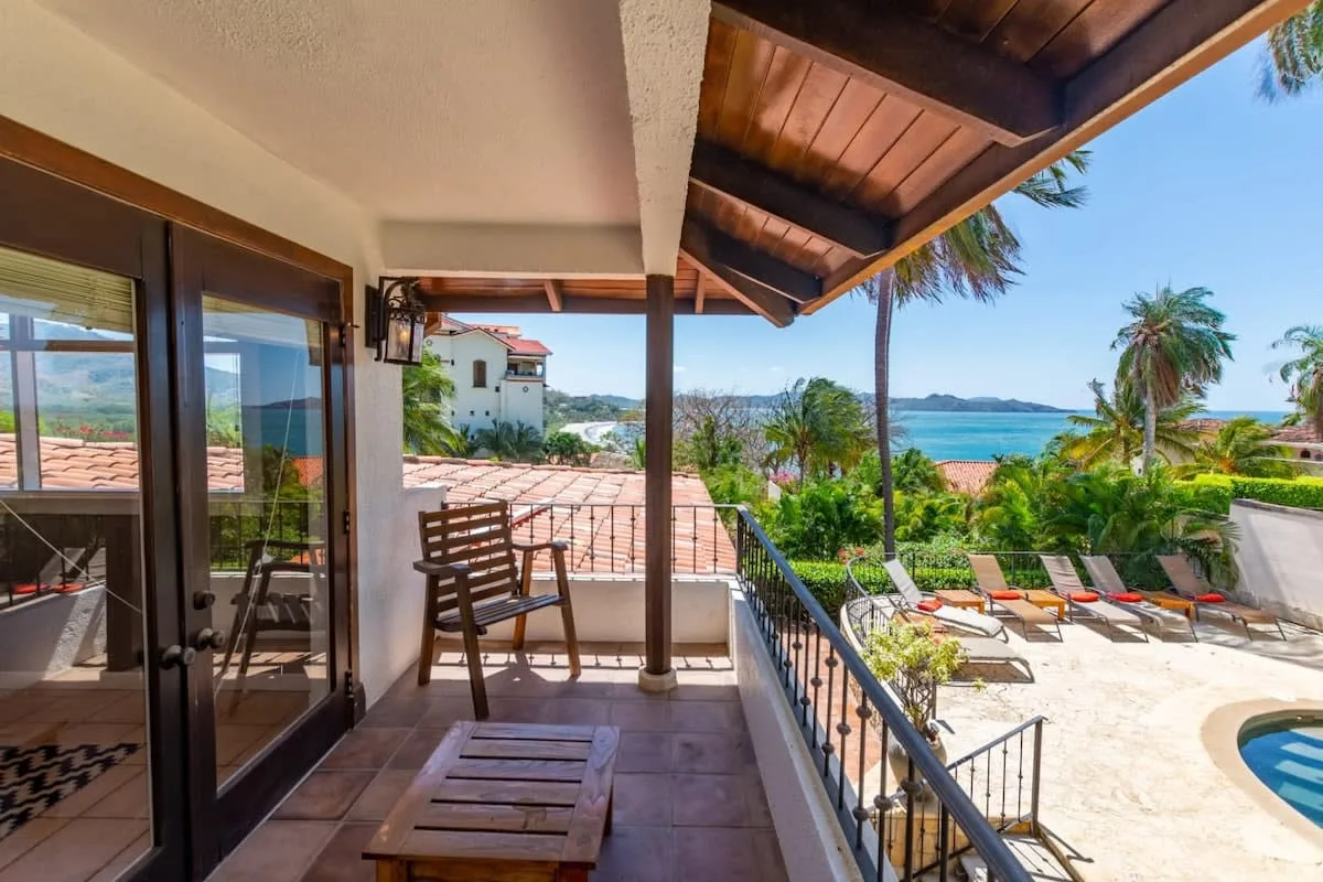A covered terrace overlooks a garden, swimming pool, and ocean.