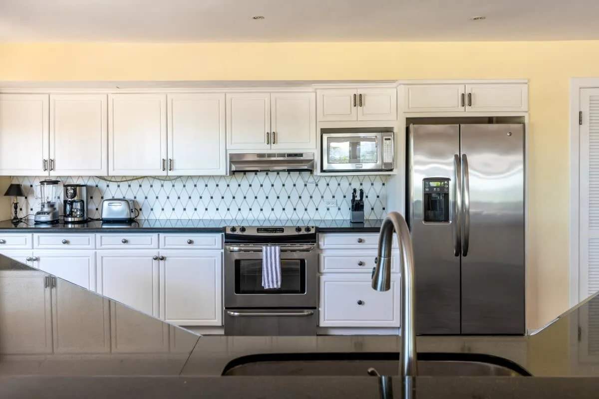 A bright kitchen with white cabinets, stainless steel appliances, and a tiled backsplash.