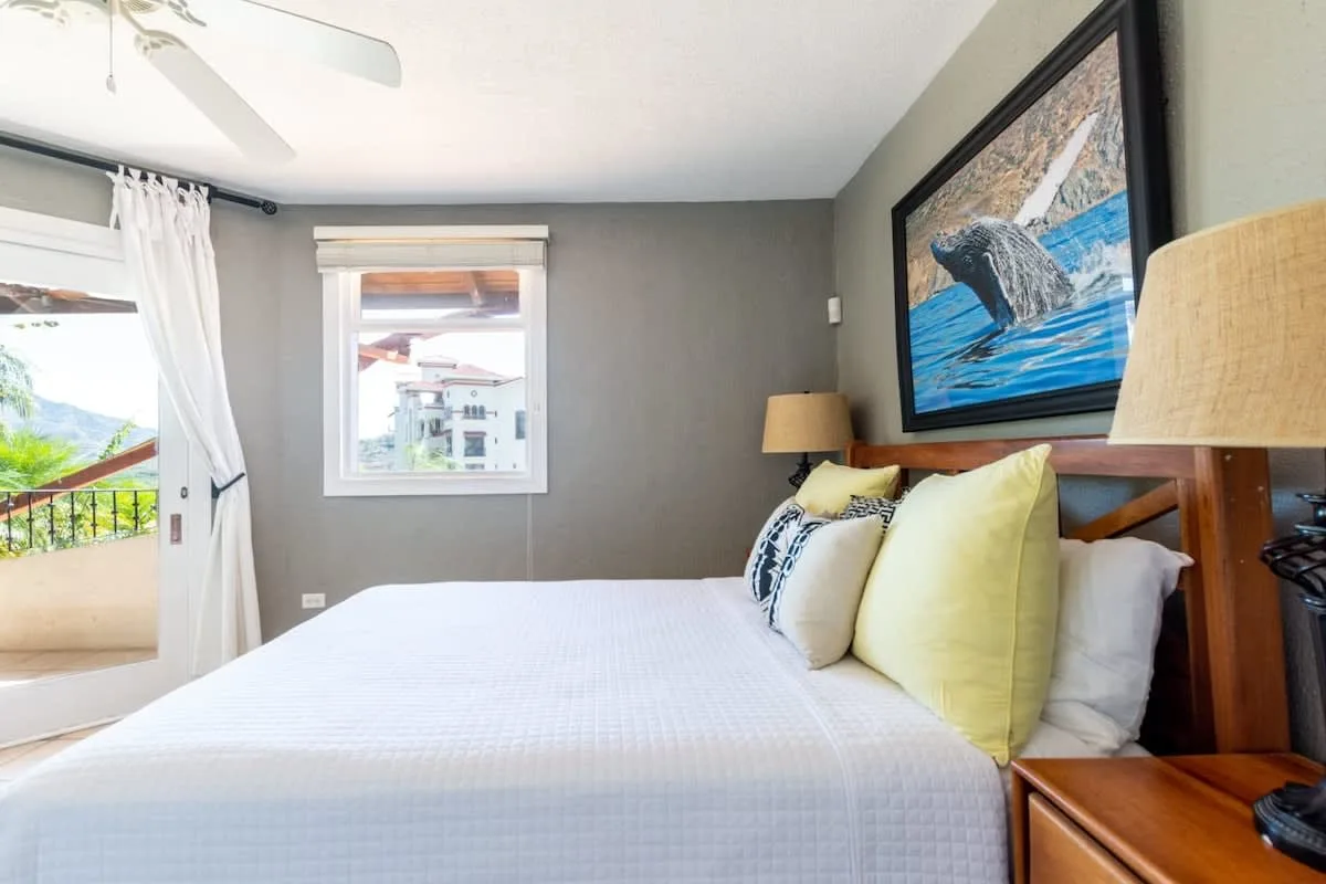 A bedroom with a neatly made bed and framed ocean artwork above the headboard.