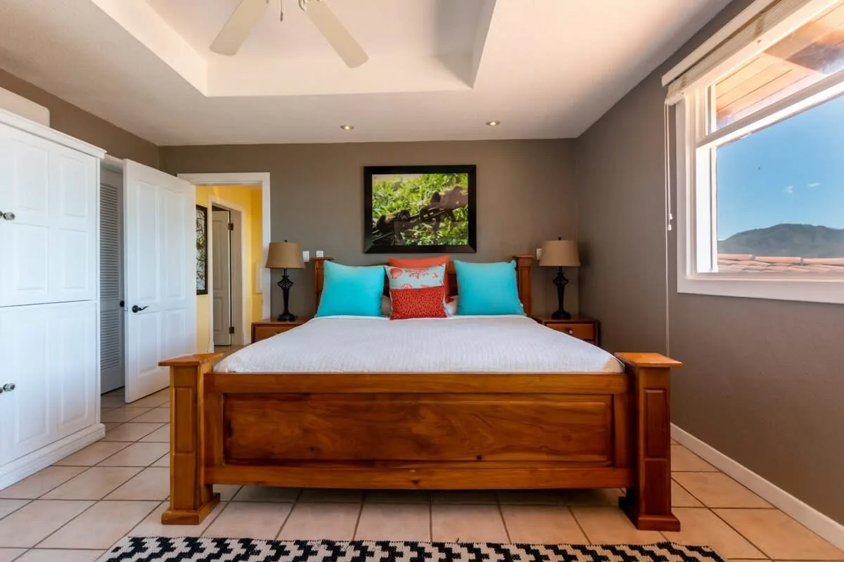 A bedroom with a wooden bed, colorful pillows, and a large window.