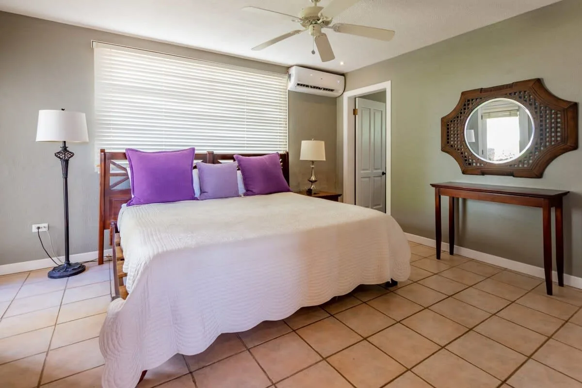 A bedroom with a bed, purple pillows, and a mirror above a wooden table.
