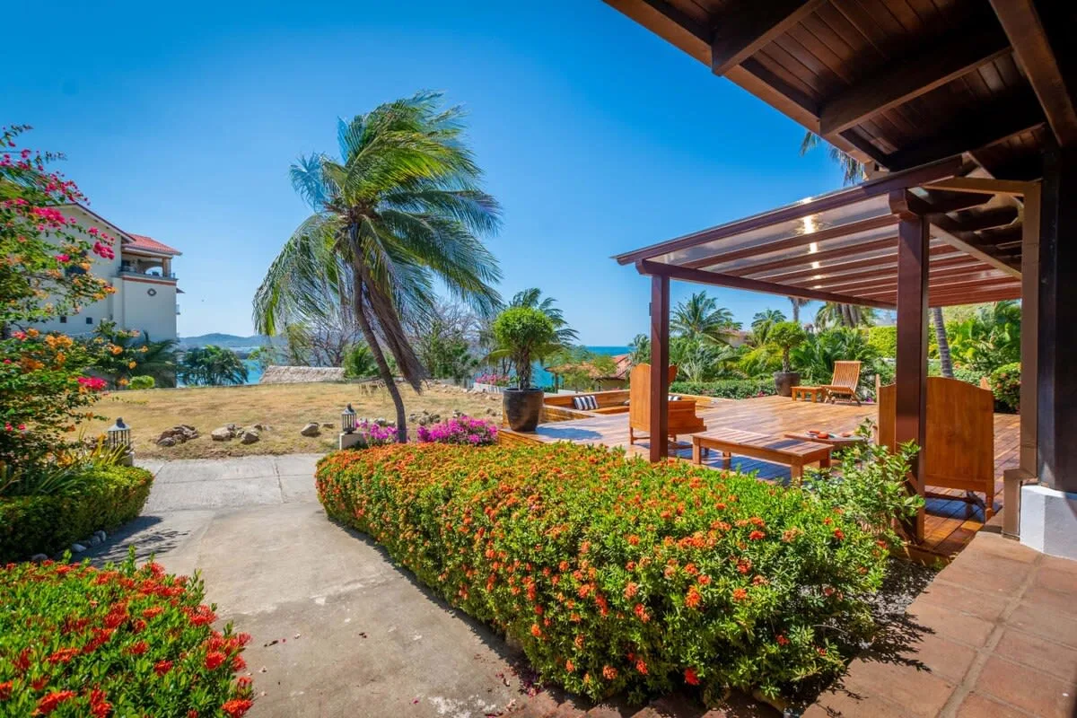 A tropical garden path leads to a wooden patio beside the sea.