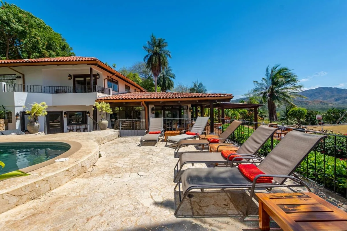 A sunny outdoor pool terrace with lounge seating and palm trees.