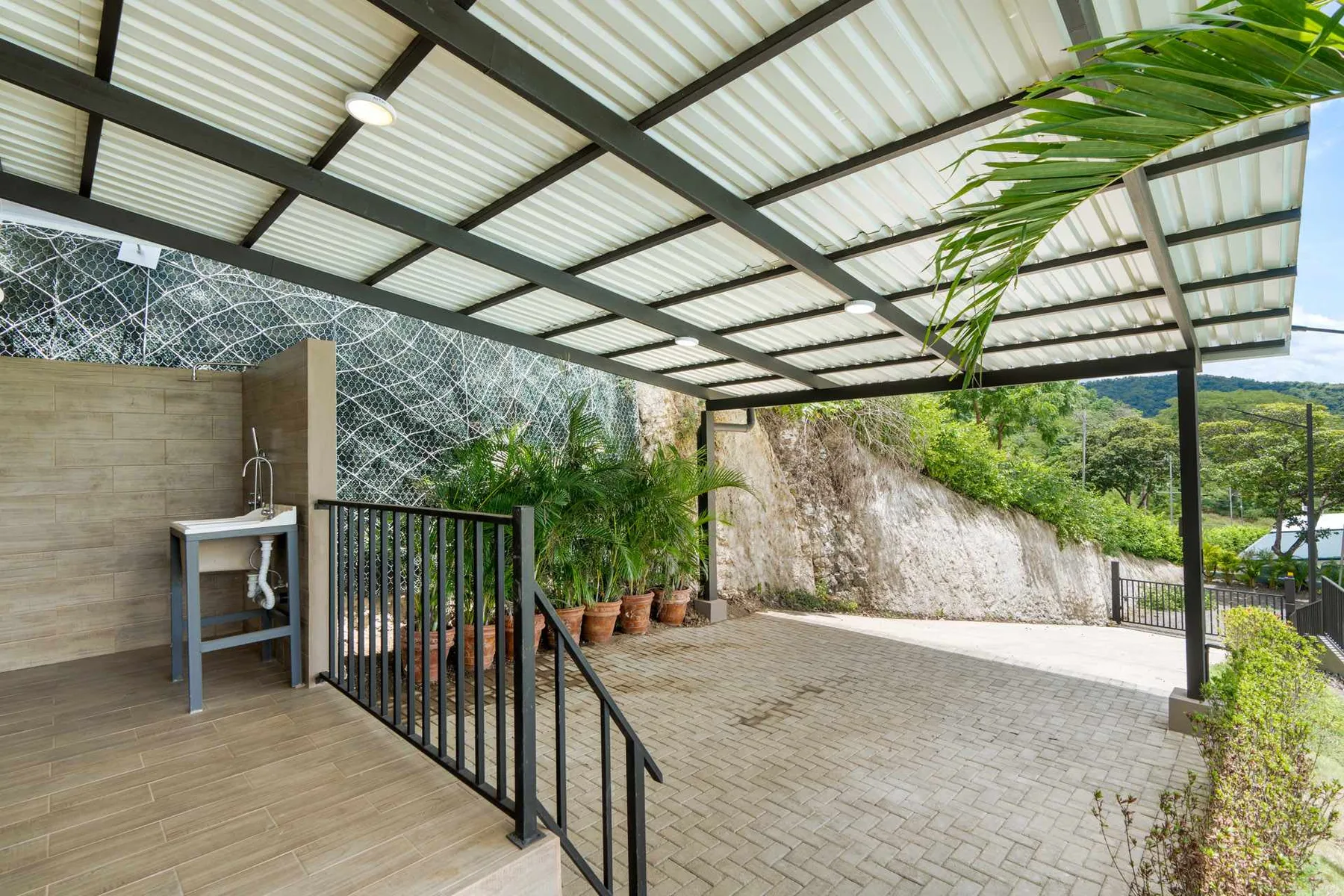 A covered patio with a tiled floor, potted plants, and a black railing.
