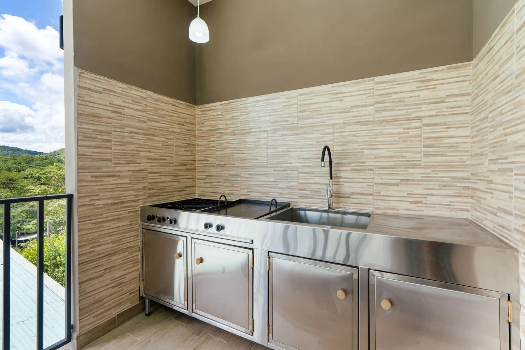 A kitchen counter with a sink and tiled walls beside an open window.