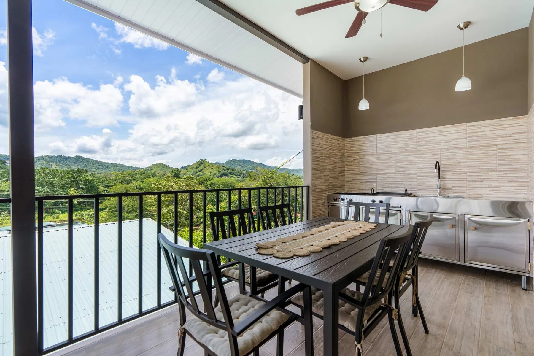 A covered dining area with a table and chairs overlooks green hills.