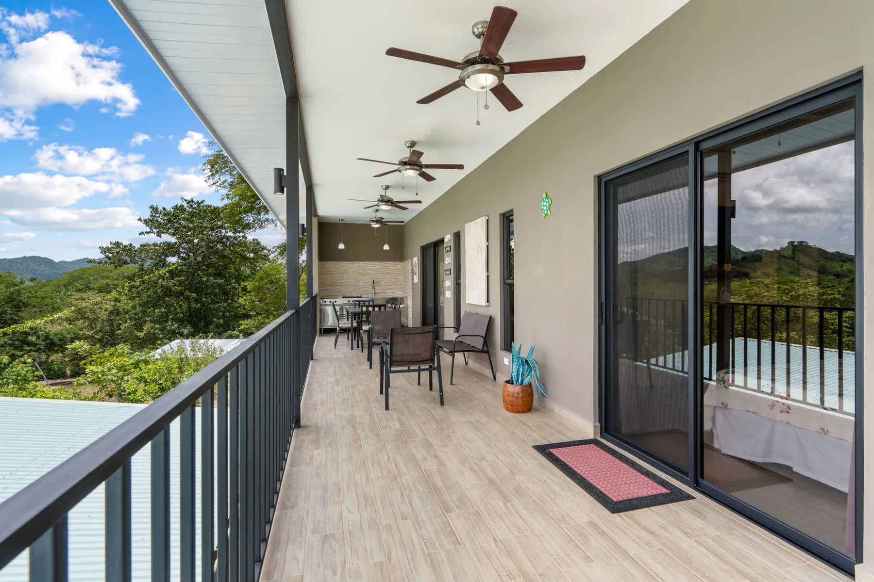 A covered outdoor balcony with seating and sliding glass doors overlooks green hills.