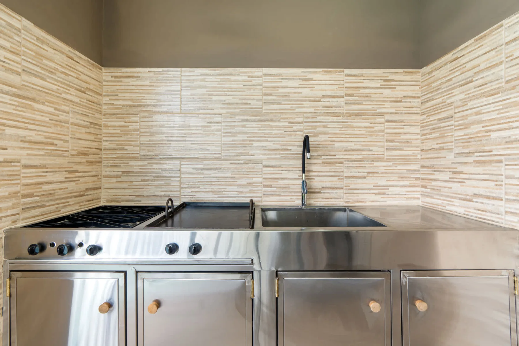 A stainless-steel kitchen stove and sink sit beneath a tiled backsplash.