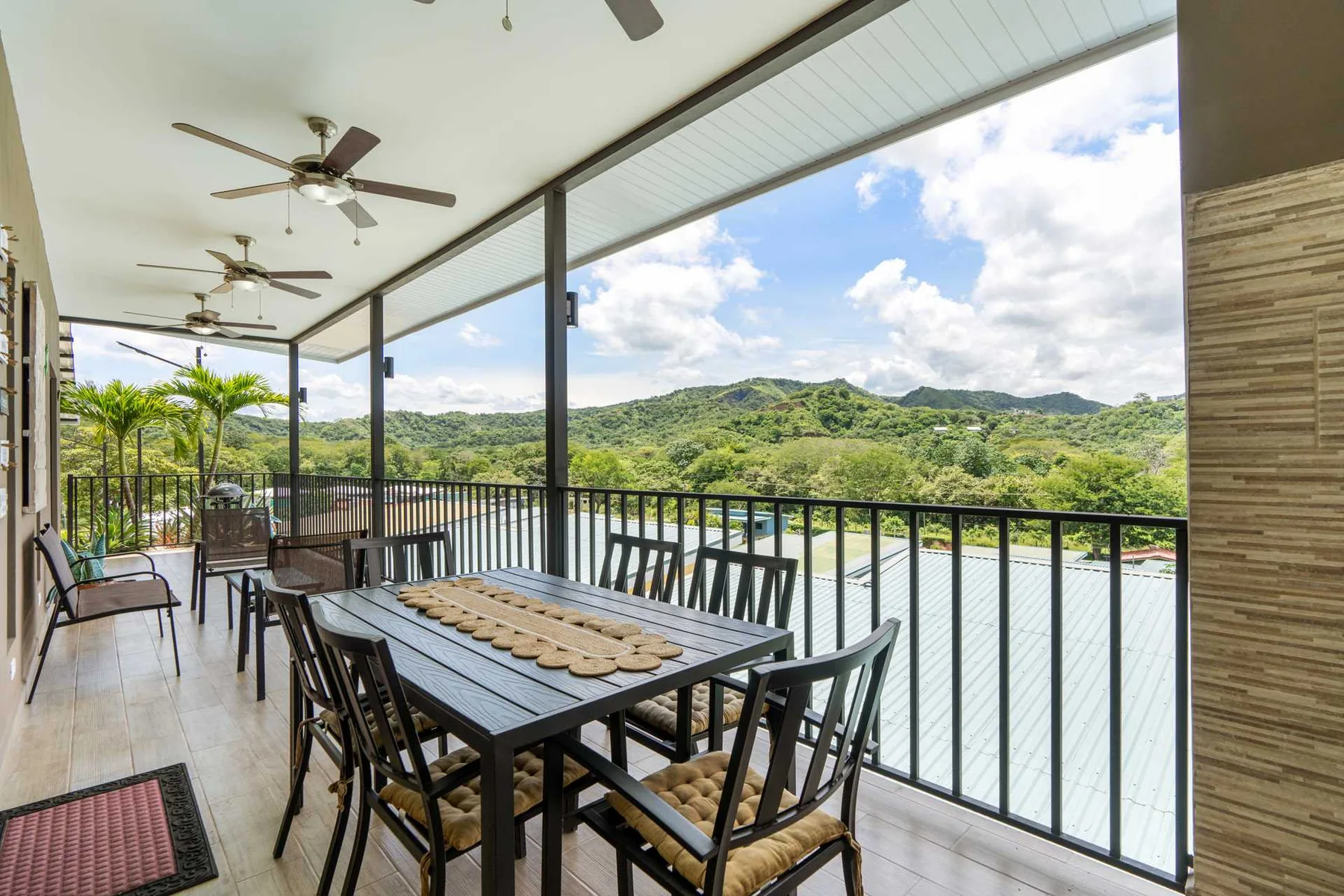 A covered outdoor dining area with a table and a view of green hills.