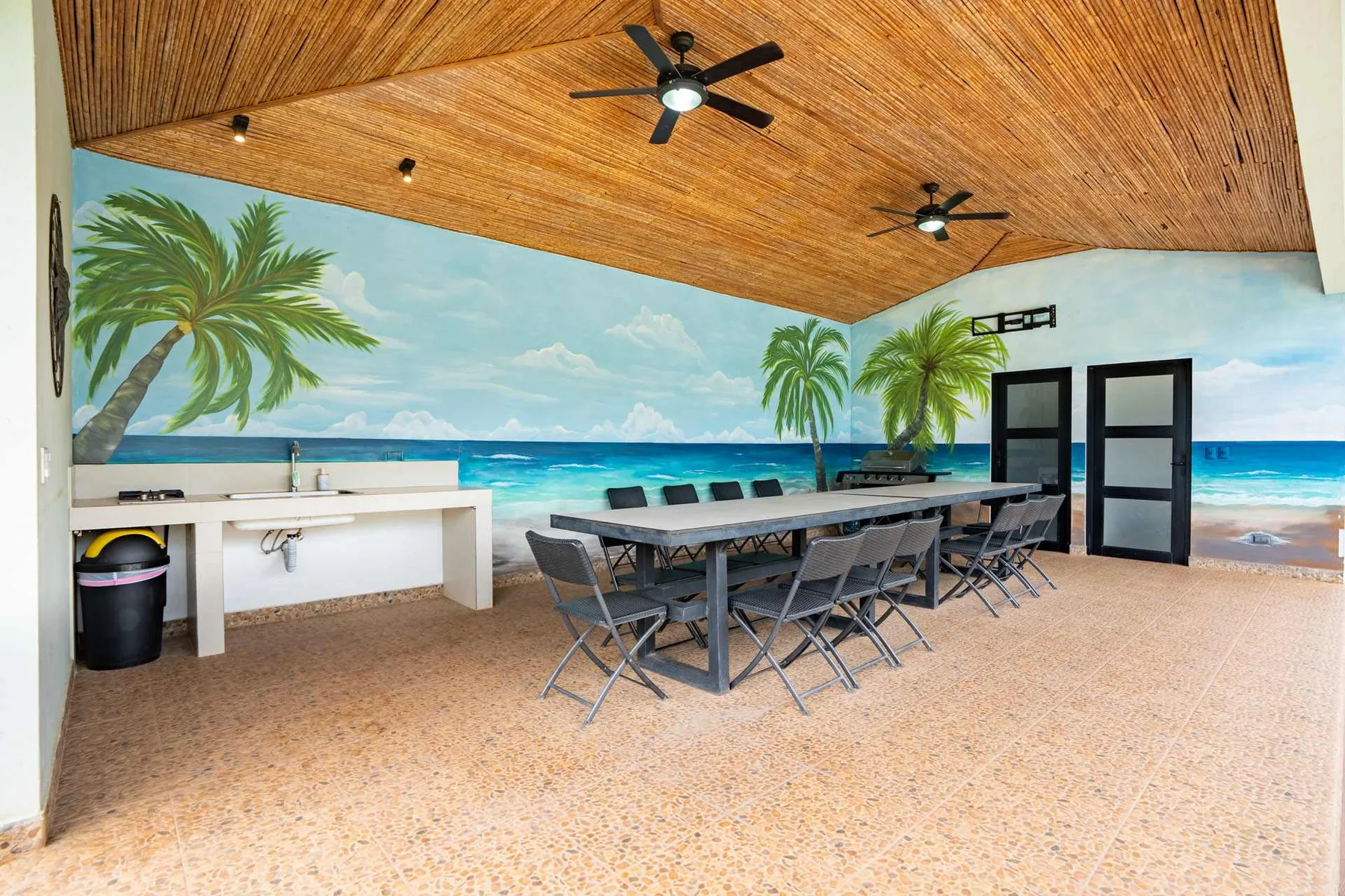 Shared amenity: A covered dining area with a long table and a tropical beach mural.