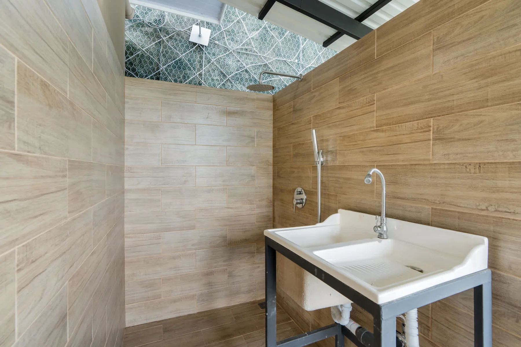 A tiled bathroom with a white washbasin and shower fixtures.