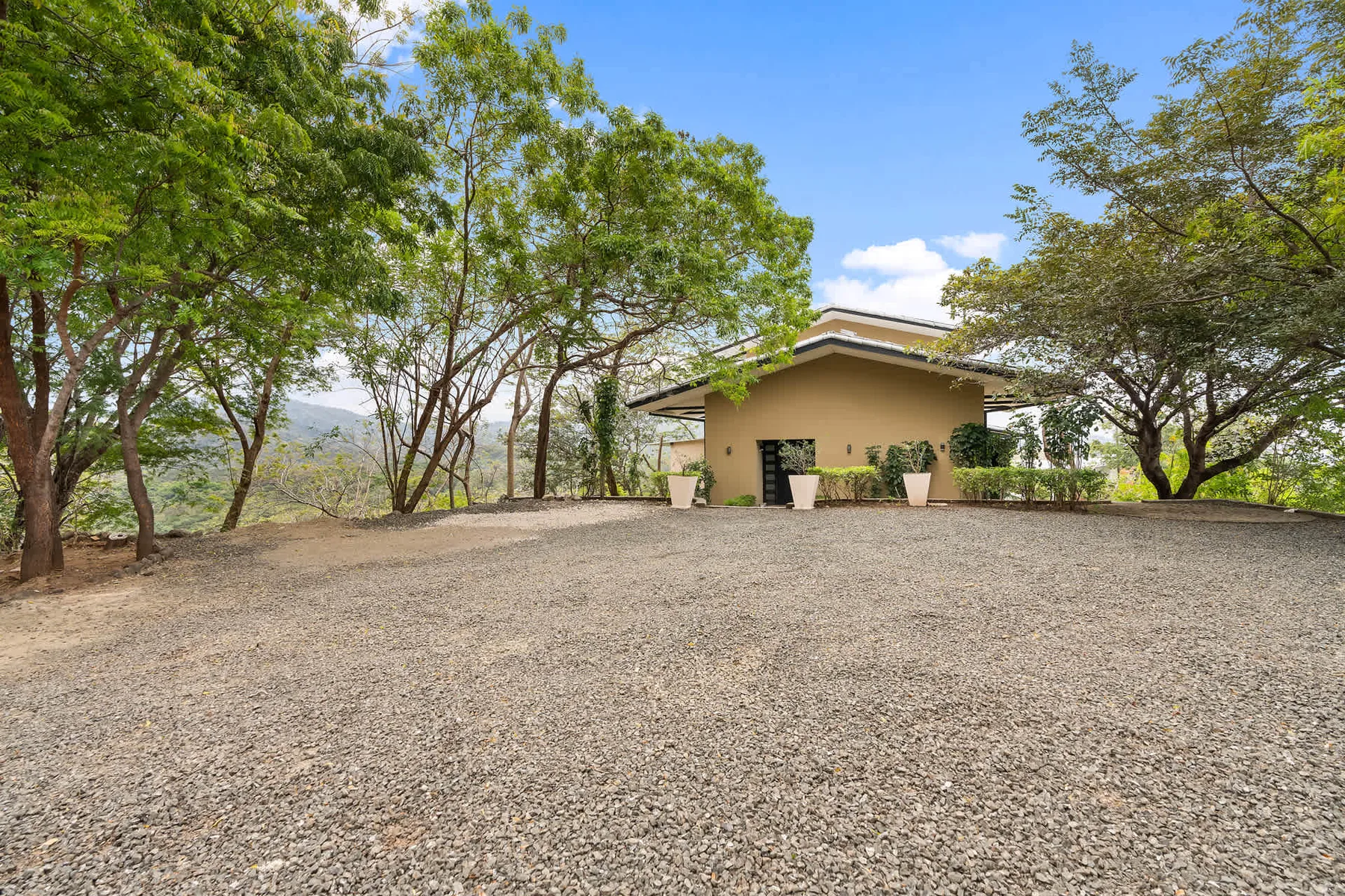 A small building stands beyond a broad gravel clearing among trees.