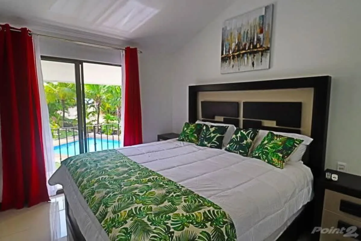 Un dormitorio con una cama grande y ropa de cama con estampado de hojas junto a una puerta de vidrio.