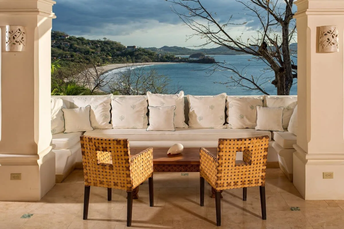 A cushioned outdoor seating area overlooks a bay beneath a cloudy sky.