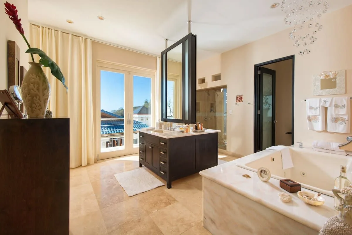 A bright bathroom features a central vanity, a bathtub, and tall windows.