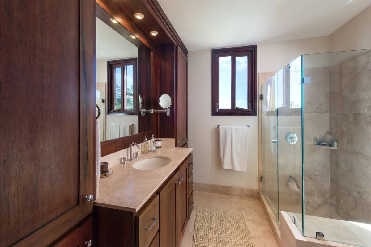 A bathroom with a wood vanity, a window, and a glass shower.