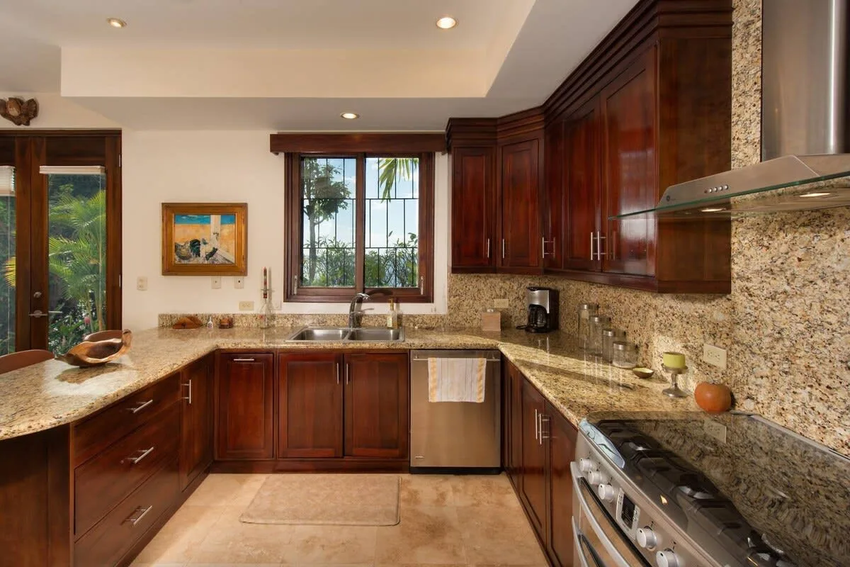 A kitchen with dark wood cabinets, stone countertops, and a window above the sink.