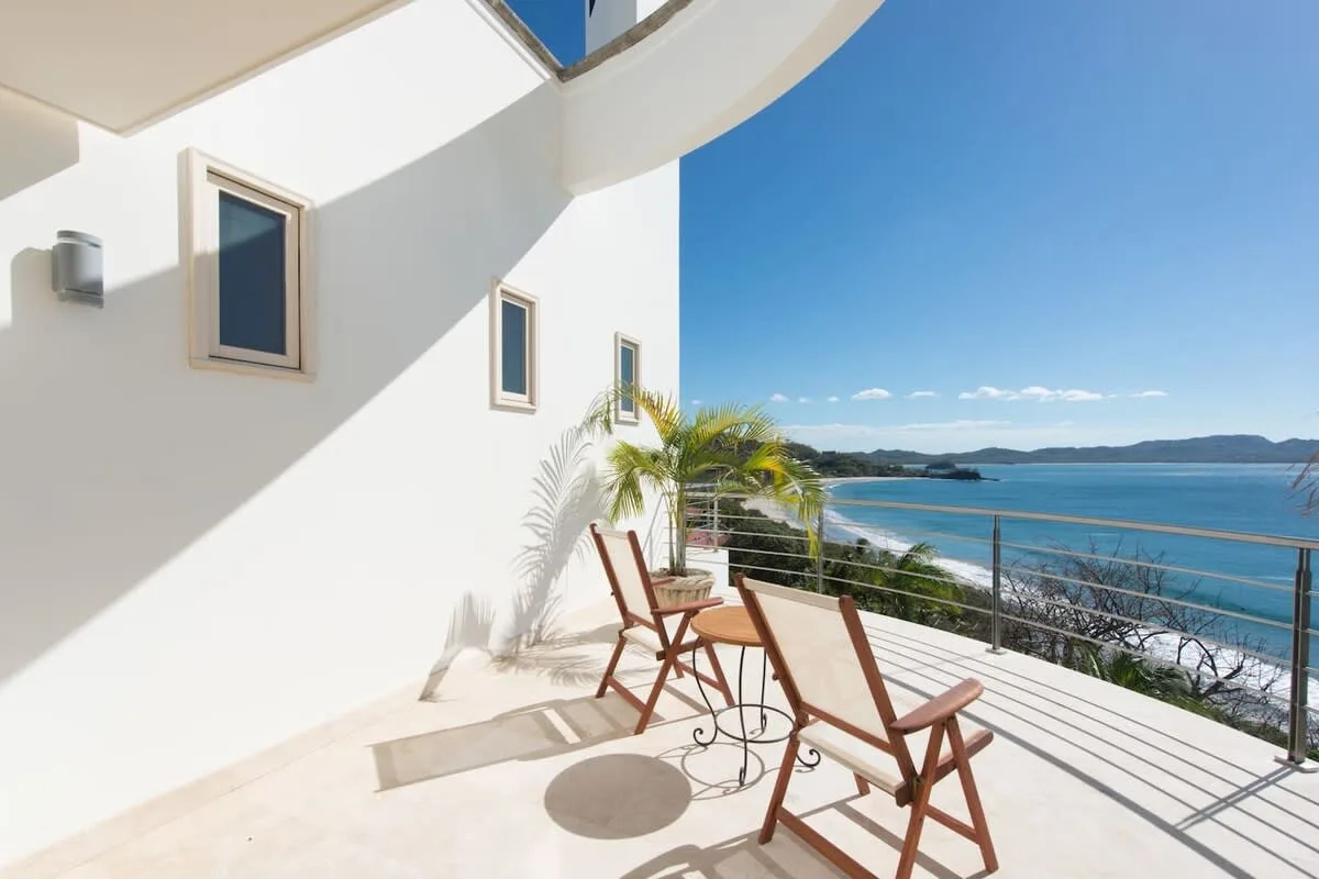 A sunlit terrace with seating overlooks the water.
