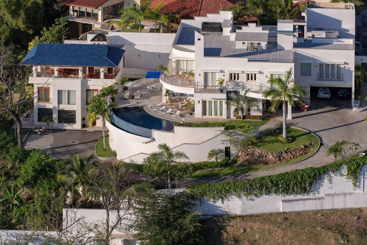 A modern multi-building property with a curved pool and surrounding gardens.