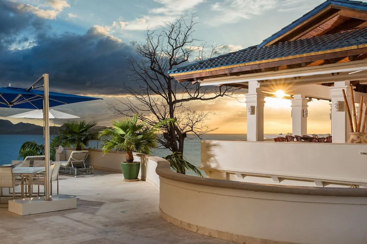 An outdoor patio with seating and a covered structure overlooking the sunset.