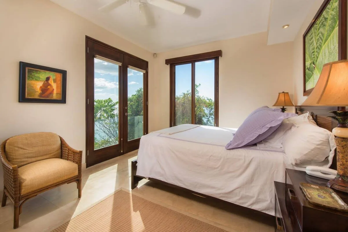A bedroom with a bed, an armchair, and tall windows.