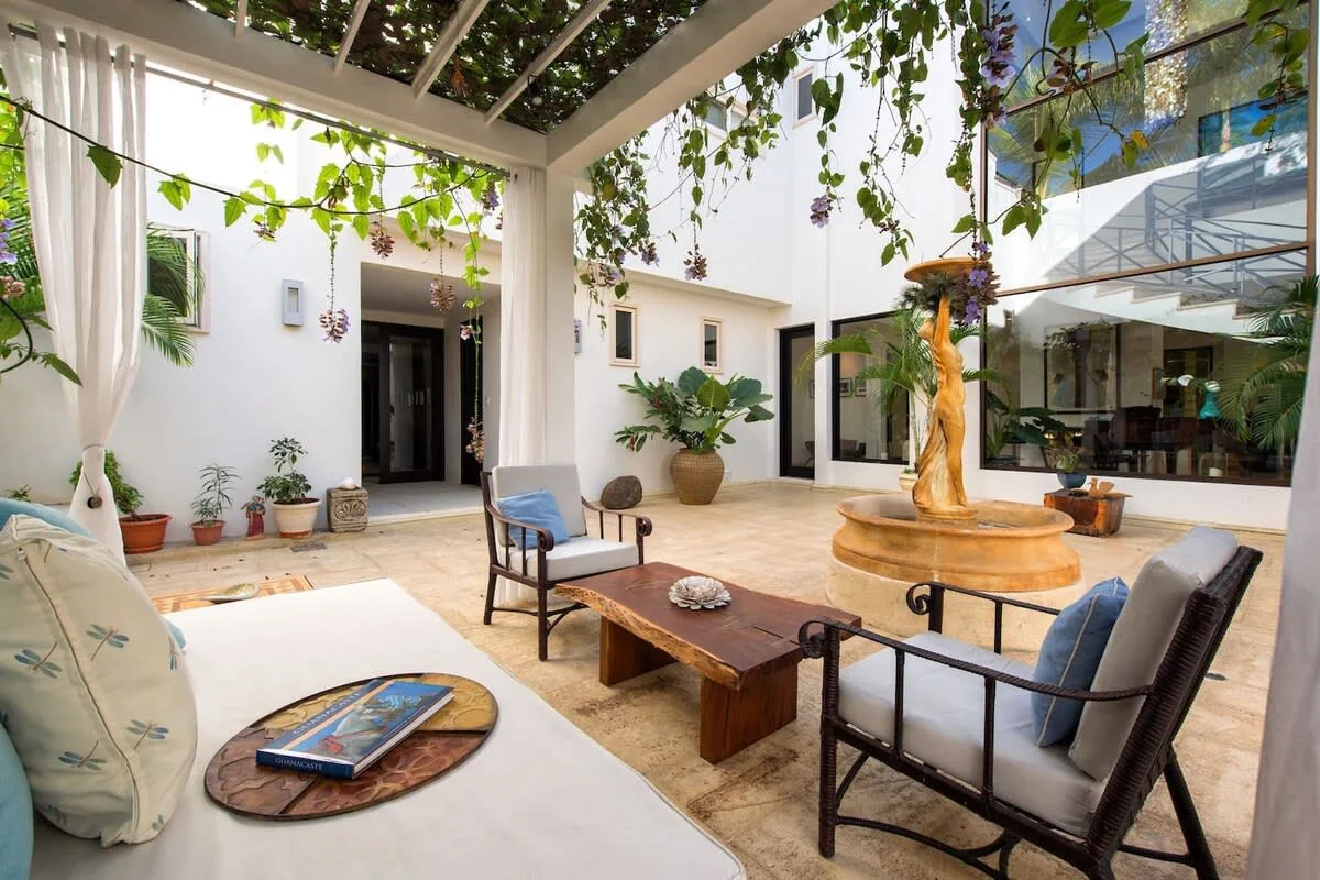 An open-air courtyard lounge with seating beneath a leafy pergola.
