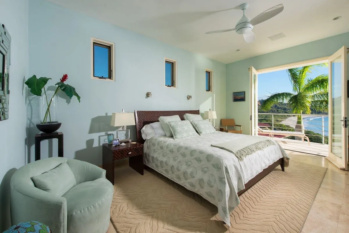 A bright bedroom with a large bed and open doors to a balcony.